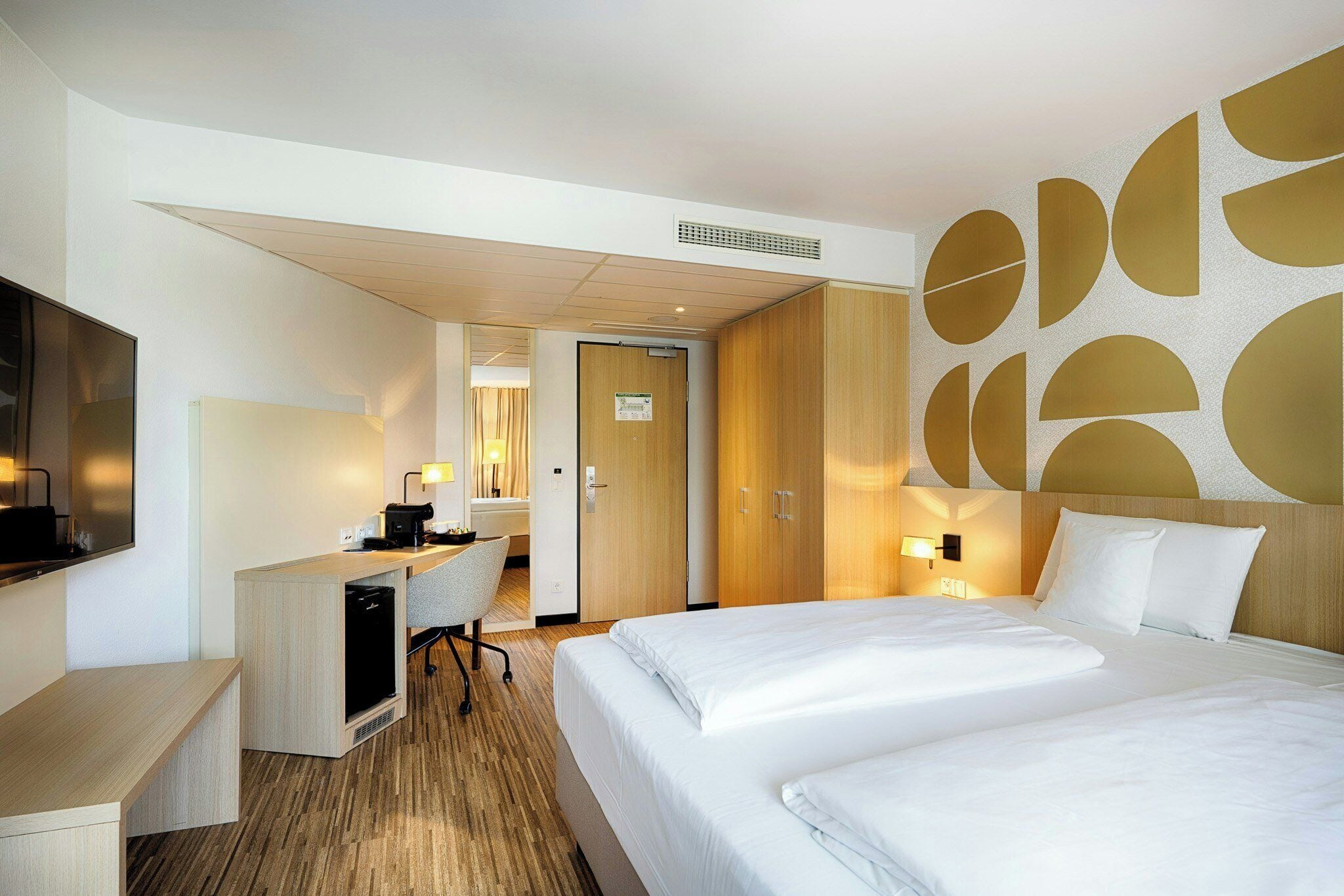 A hotel room with a bed, a desk with a computer, a chair, and a TV.
