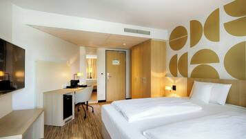 A hotel room with a bed, a desk with a computer, a chair, and a TV.