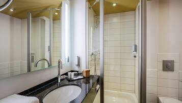Un baño moderno con ducha envuelta en vidrio, un lavamanos blanco y un espejo grande.