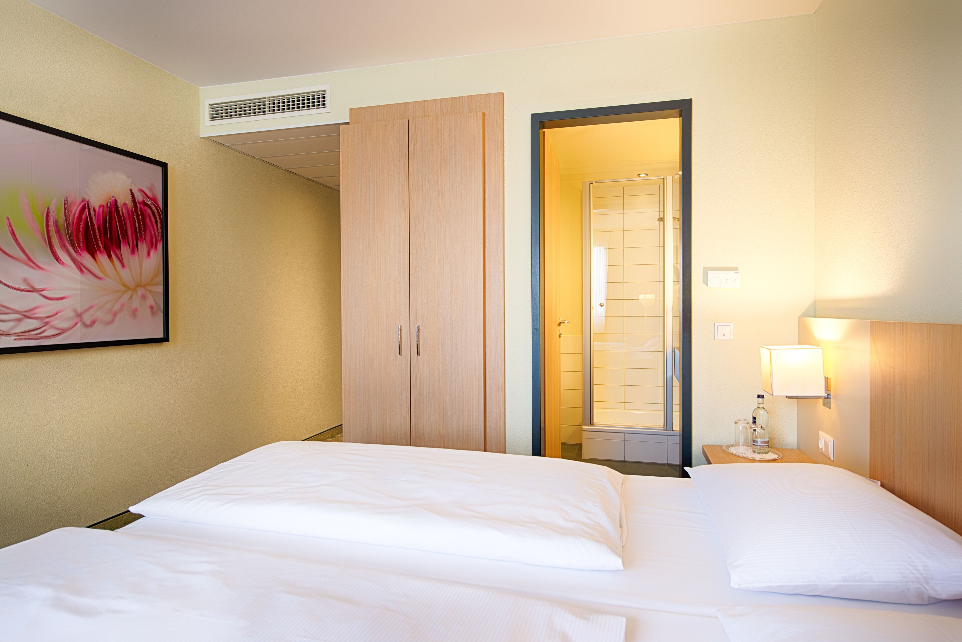 A hotel room with a bed, a wardrobe, a bathroom, and a painting on the wall.