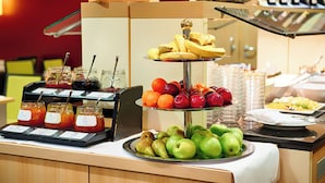 A buffet with various fruits, including apples, oranges, and bananas, and several jars of jam. - Welcome Hotel Paderborn (Paderborn)