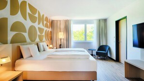 A hotel room with a large bed, a TV, a desk, and a chair. - Welcome Hotel Paderborn (Paderborn)
