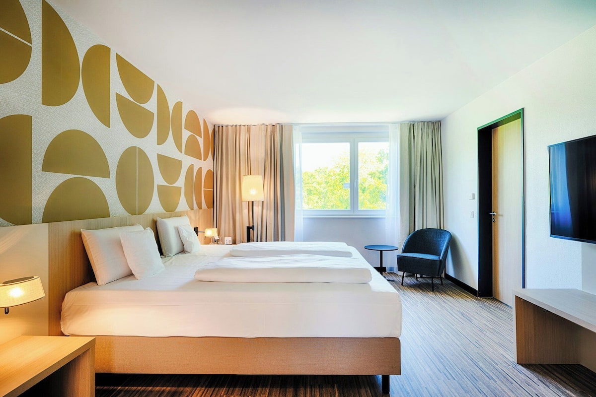 Ein Hotelzimmer mit einem großen Bett, einem Fernseher, einem Schreibtisch und einem Stuhl.
