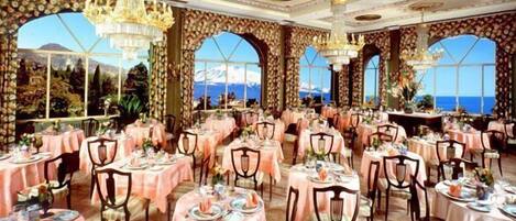A restaurant with multiple tables set for dining, large windows with a view, and ornate chandeliers.