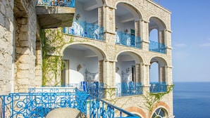 Un bâtiment en pierre, doté de balcons et d’arcades bleus, qui offre une vue sur la mer.