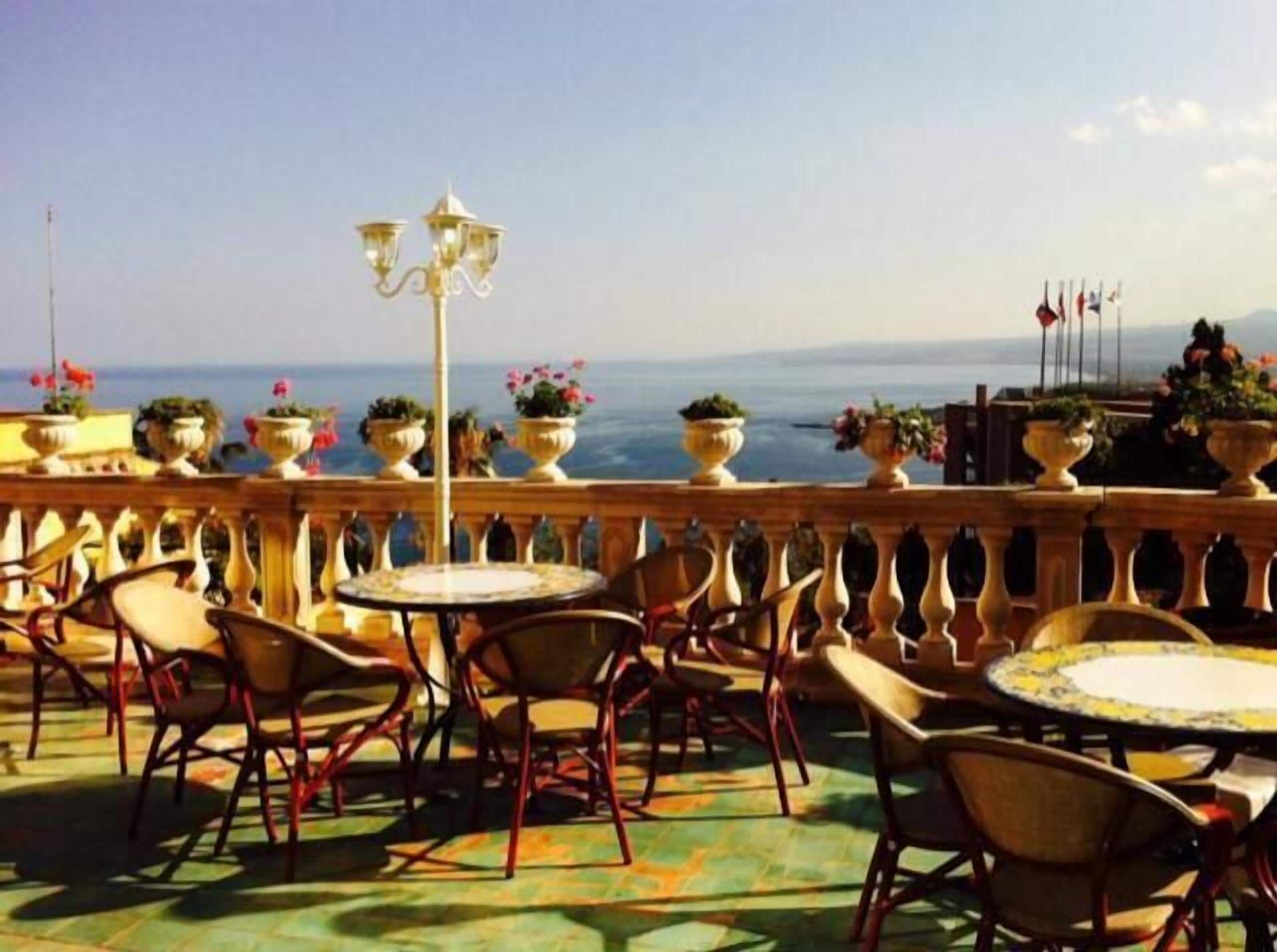 A terrace with outdoor seating, potted plants, and a view of the sea.