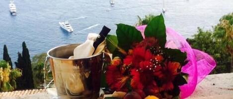 Une vue pittoresque de la mer, avec des bateaux, un seau en métal, un bouquet de fleurs et une assiette de fruits.