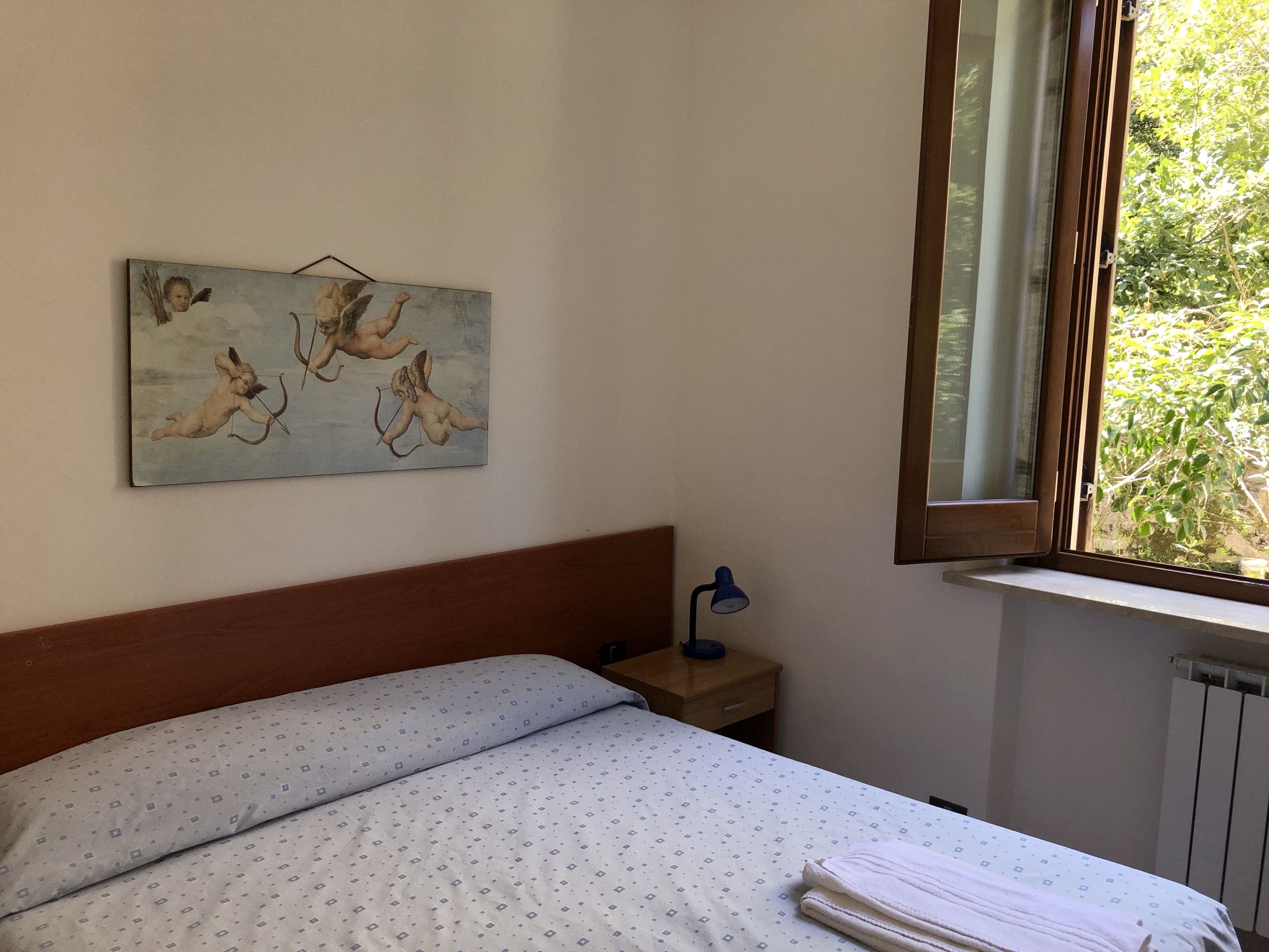 A bedroom with a bed, a nightstand, a lamp, a window, and a painting on the wall.