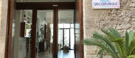 The entrance to Hotel San Giovanni with a stone wall and a signboard.