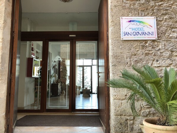 La entrada del Hotel San Giovanni, con un muro de piedra y un cartel.