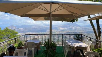 An outdoor patio with tables and chairs, a large umbrella, and a scenic mountain view.