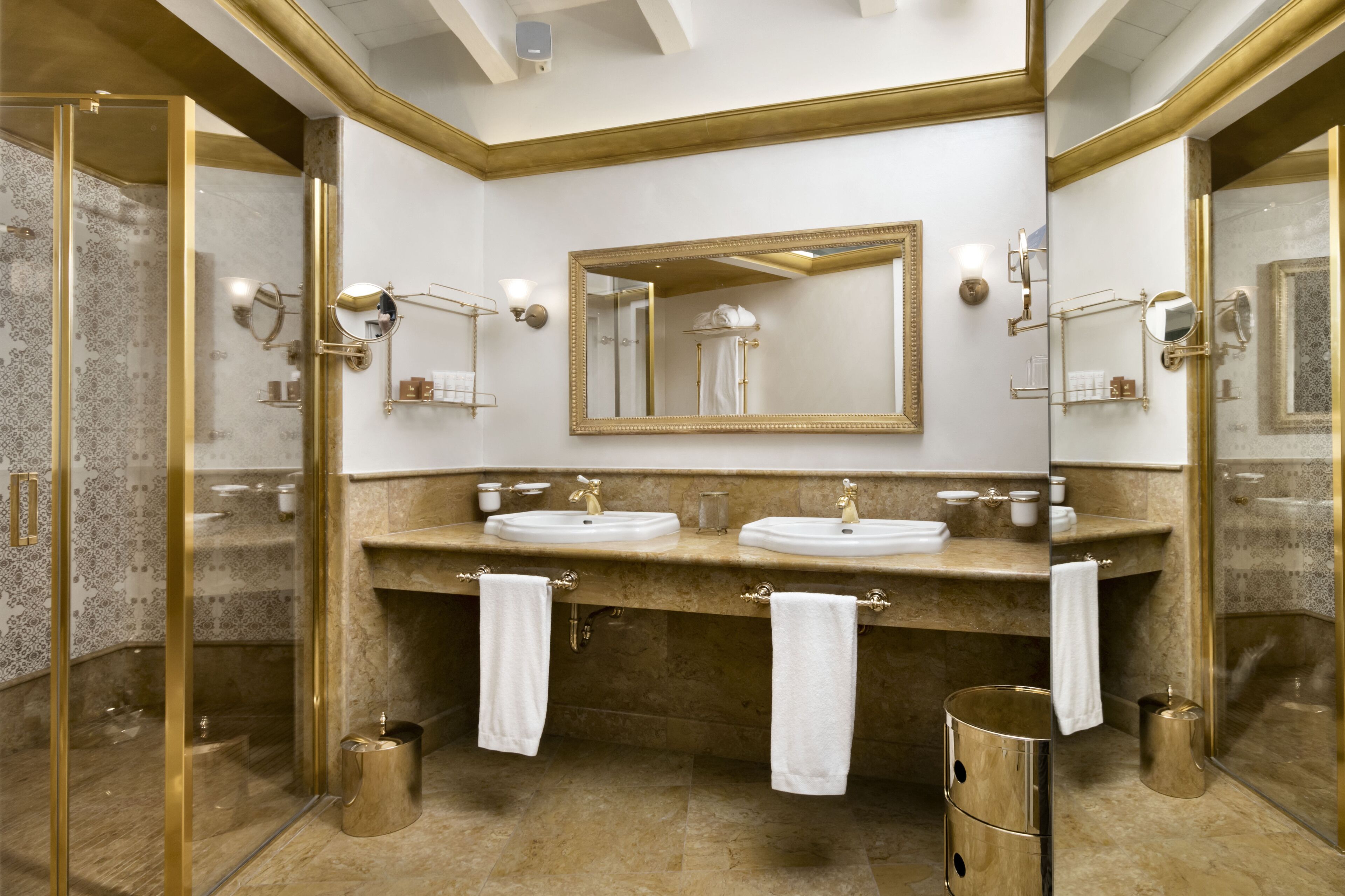 A luxurious bathroom with two sinks, a large mirror, and gold fixtures.