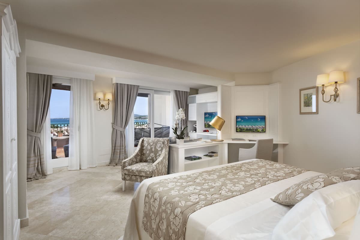 A hotel room with a bed, desk, chair, and a view of the sea.