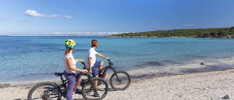 Deux personnes sur une plage, avec des vélos, sous un ciel dégagé et au large d’une mer calme.