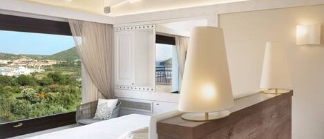 Une chambre à coucher avec un grand lit, une tête de lit en bois, une table de chevet avec des lampes, un miroir et une vue sur un paysage verdoyant par la fenêtre.