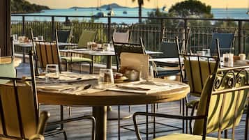 Un espace repas avec des tables et des chaises, une vue sur la mer et une balustrade de balcon.