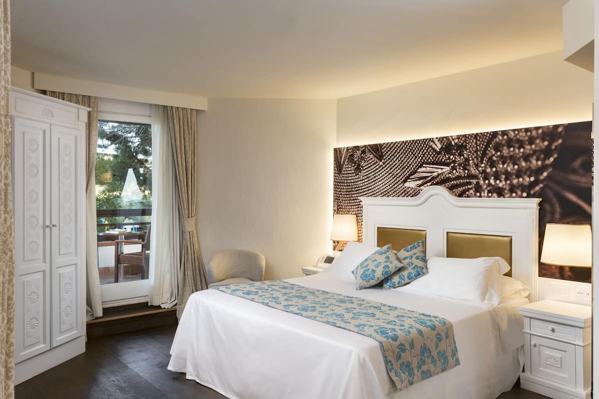 A hotel room with a large bed, a window with curtains, a white wardrobe, and a wall-mounted artwork.