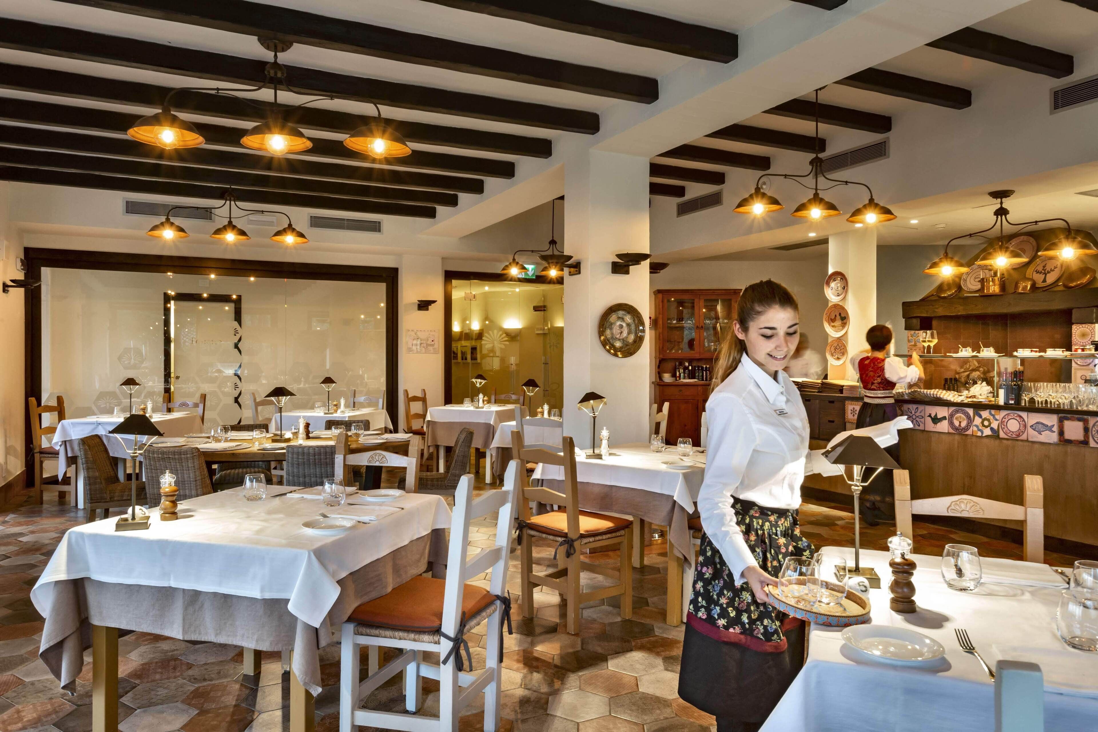 A restaurant with tables set for dining, a bar area, and a kitchen visible in the background.