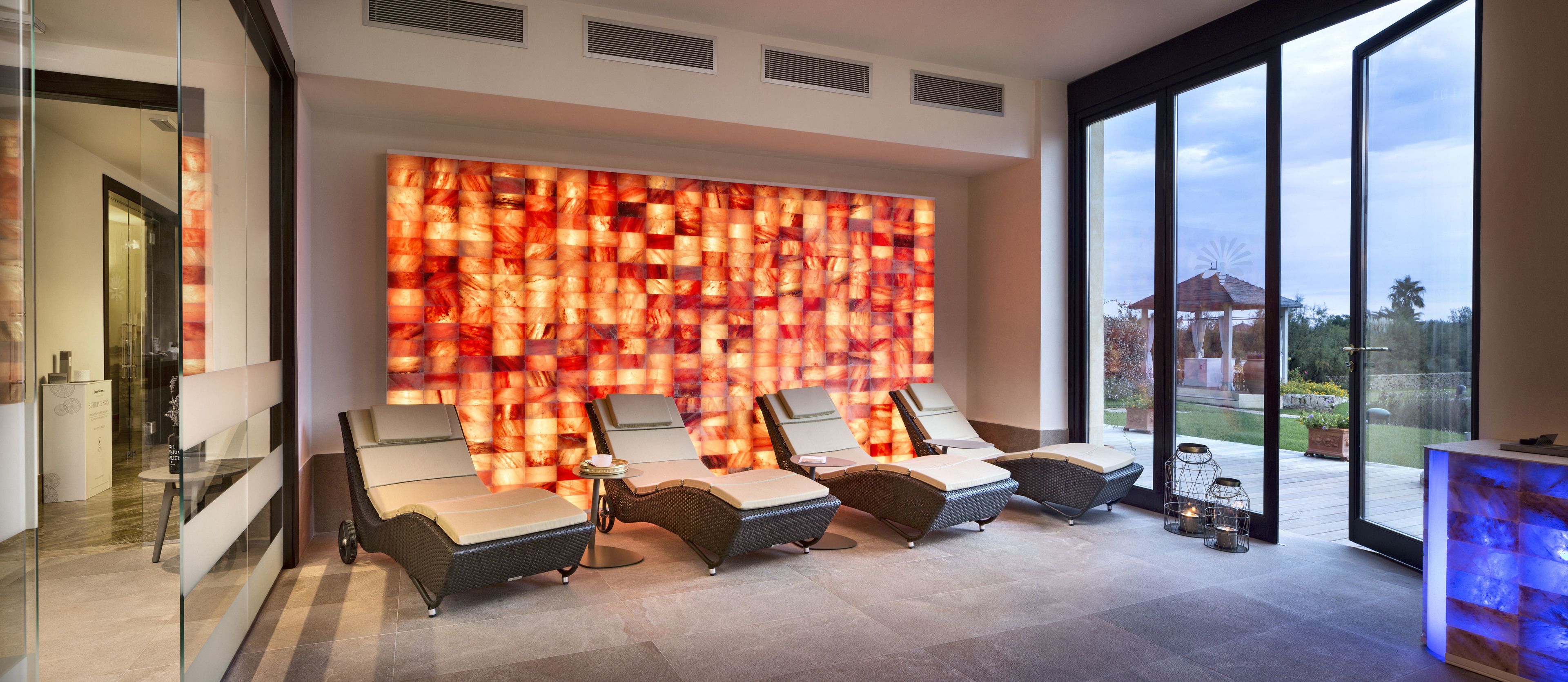 A modern lounge area with three reclining chairs, a glass partition, and a decorative wall.