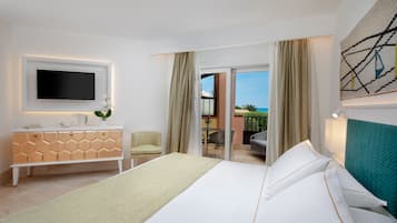Habitación de hotel con cama, televisión sobre un tocador blanco, balcón con vista al mar y un cuadro en la pared.