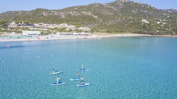 Eine Küstenlandschaft mit klarem, blauem Wasser, einem Strand und einem gebirgigen Hintergrund.