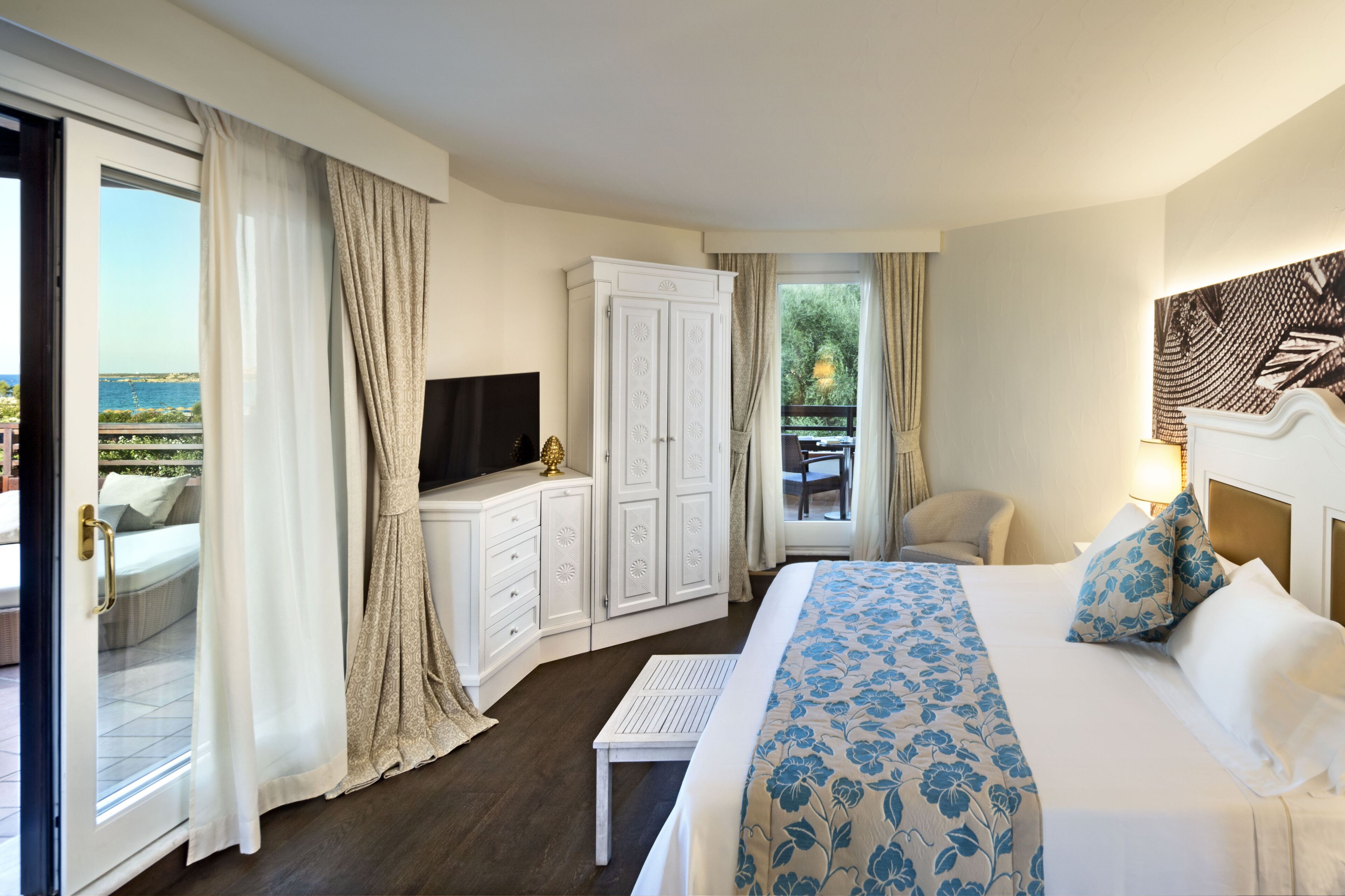 A hotel room with a bed, a TV, a wardrobe, and a balcony with a view of the sea.