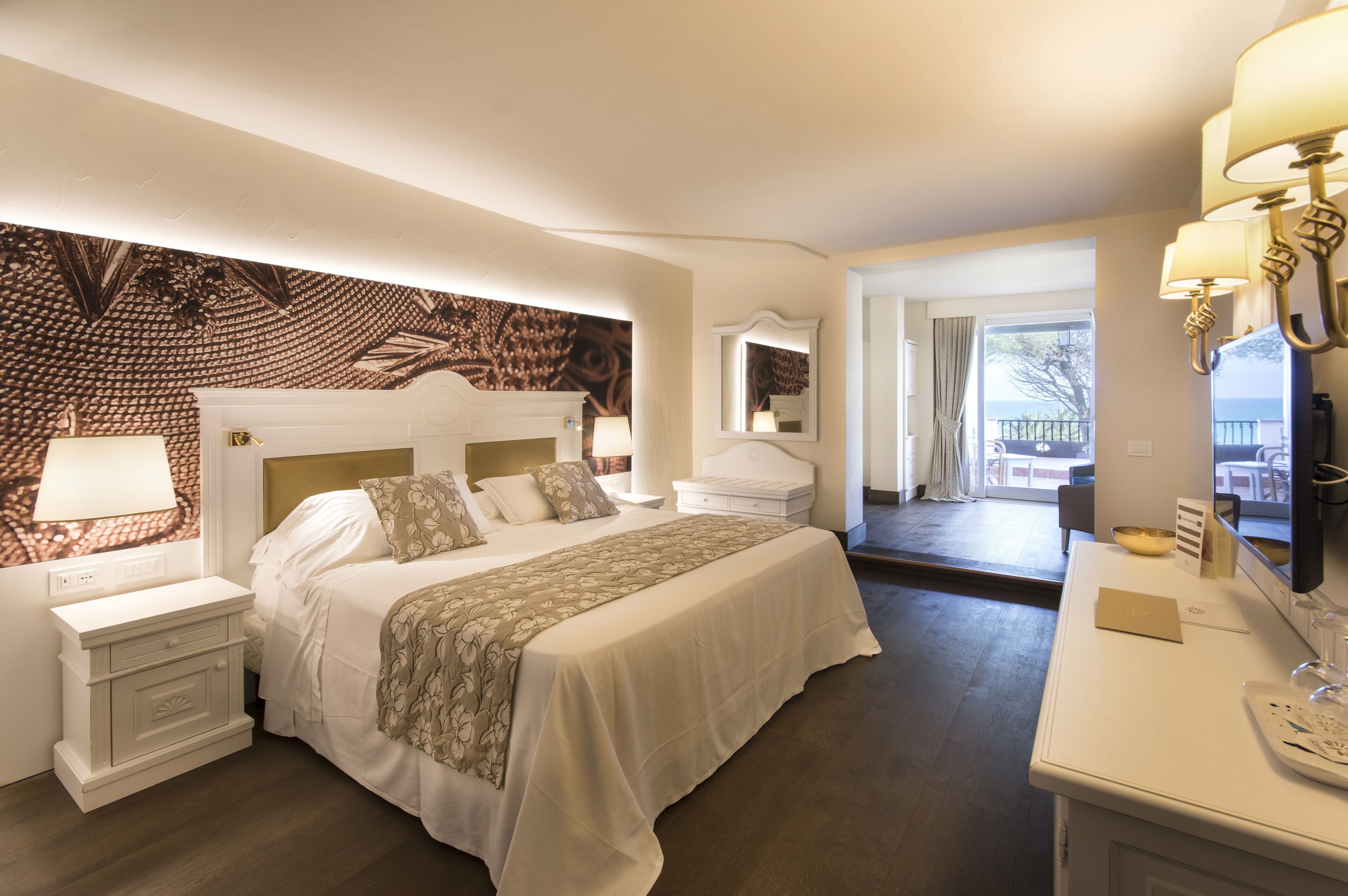 A hotel room with a large bed, a bedside table with a lamp, a dresser, and a large mirror.