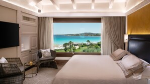 A hotel room with a large bed, a TV, a seating area with chairs, and a view of the sea. - Abi d'Oru Sardinian Beach Resort & Spa (Olbia)