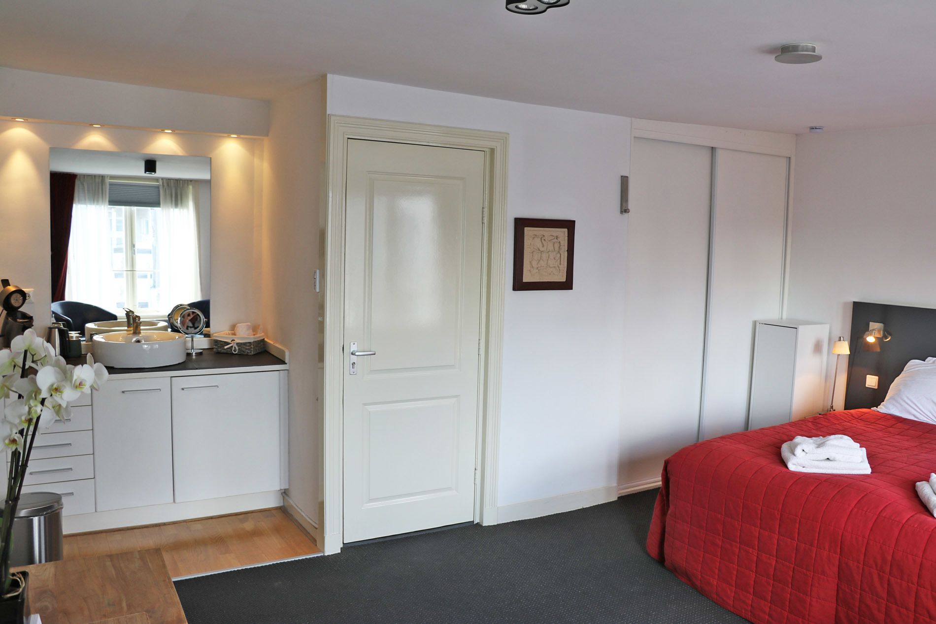 Een hotelkamer met een bed, een bureau met een wastafel, een spiegel en een ingelijst schilderij aan de muur.