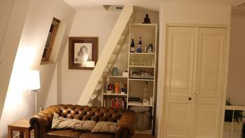 Una sala de estar con un sofá de cuero marrón, una estantería, una puerta blanca y un cuadro en la pared.