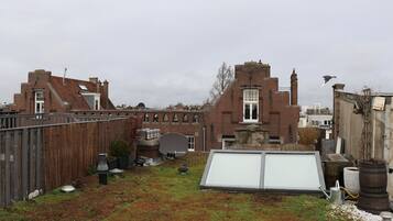 A rooftop with a large white screen, a wooden fence, and a brick building in the background.