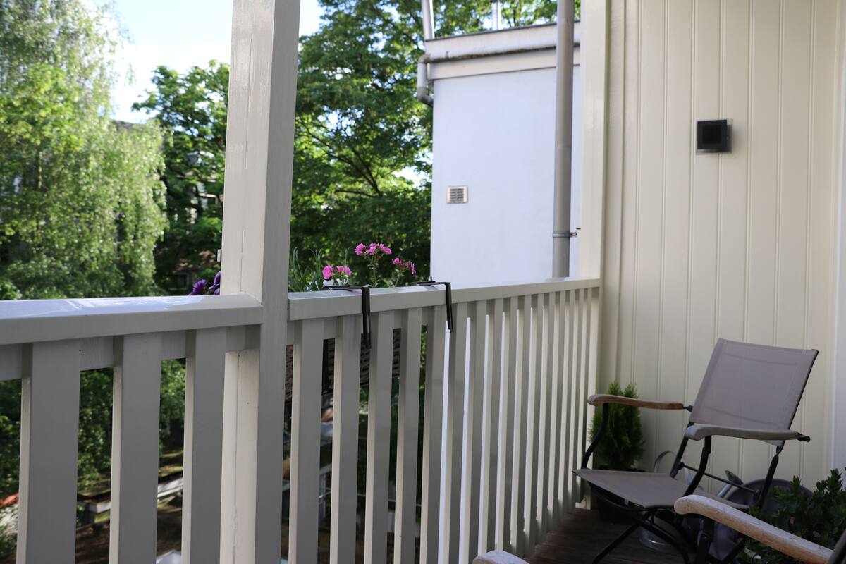 A wooden deck with a white railing, a folding chair, and a potted plant.