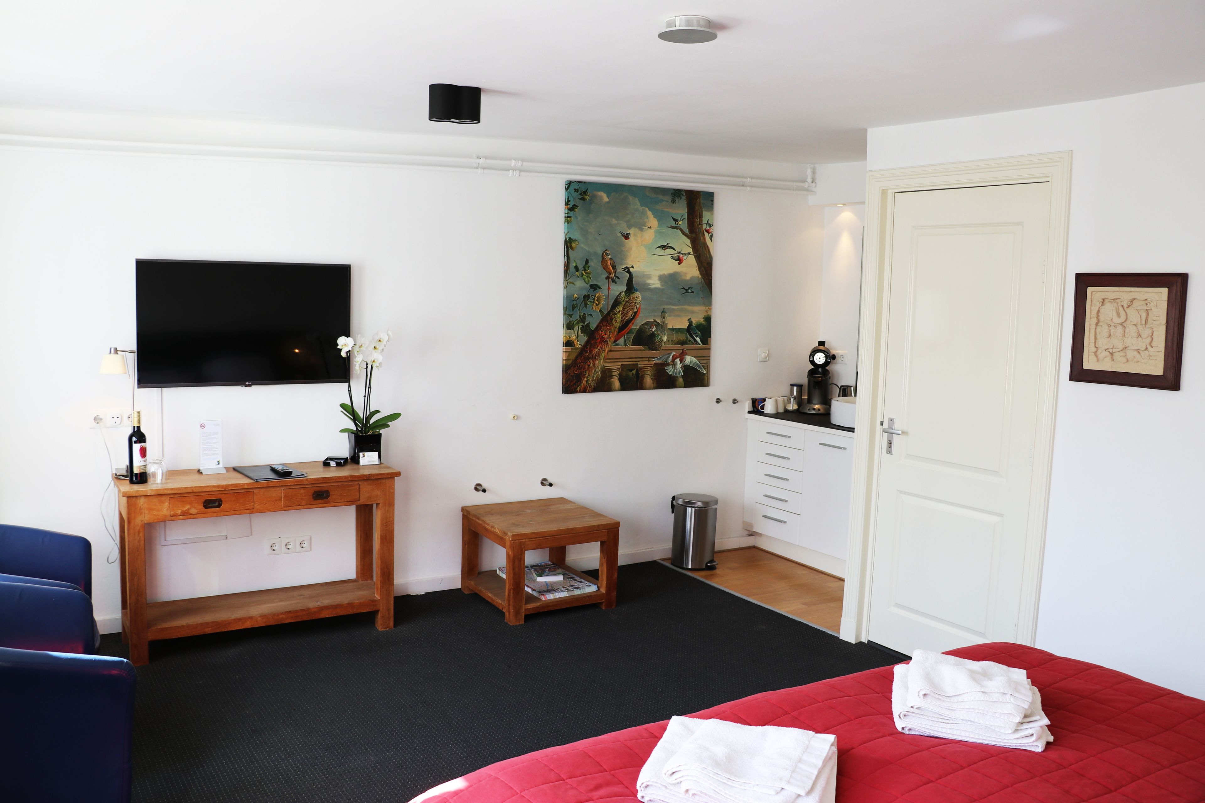 Ein Hotelzimmer mit Bett, Schreibtisch mit Computer, Fernseher, einem kleinen Tisch, einem Papierkorb und einer Tür.