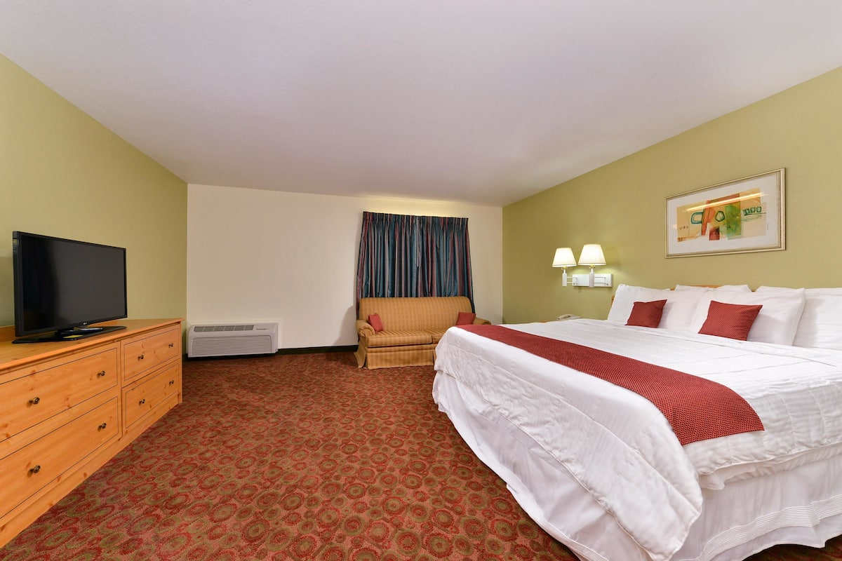 A hotel room with a bed, a television on a wooden dresser, a chair, and a wall-mounted lamp.