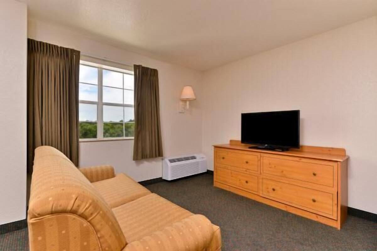 A hotel room with a sofa, a wooden dresser, a television, and a window with curtains.