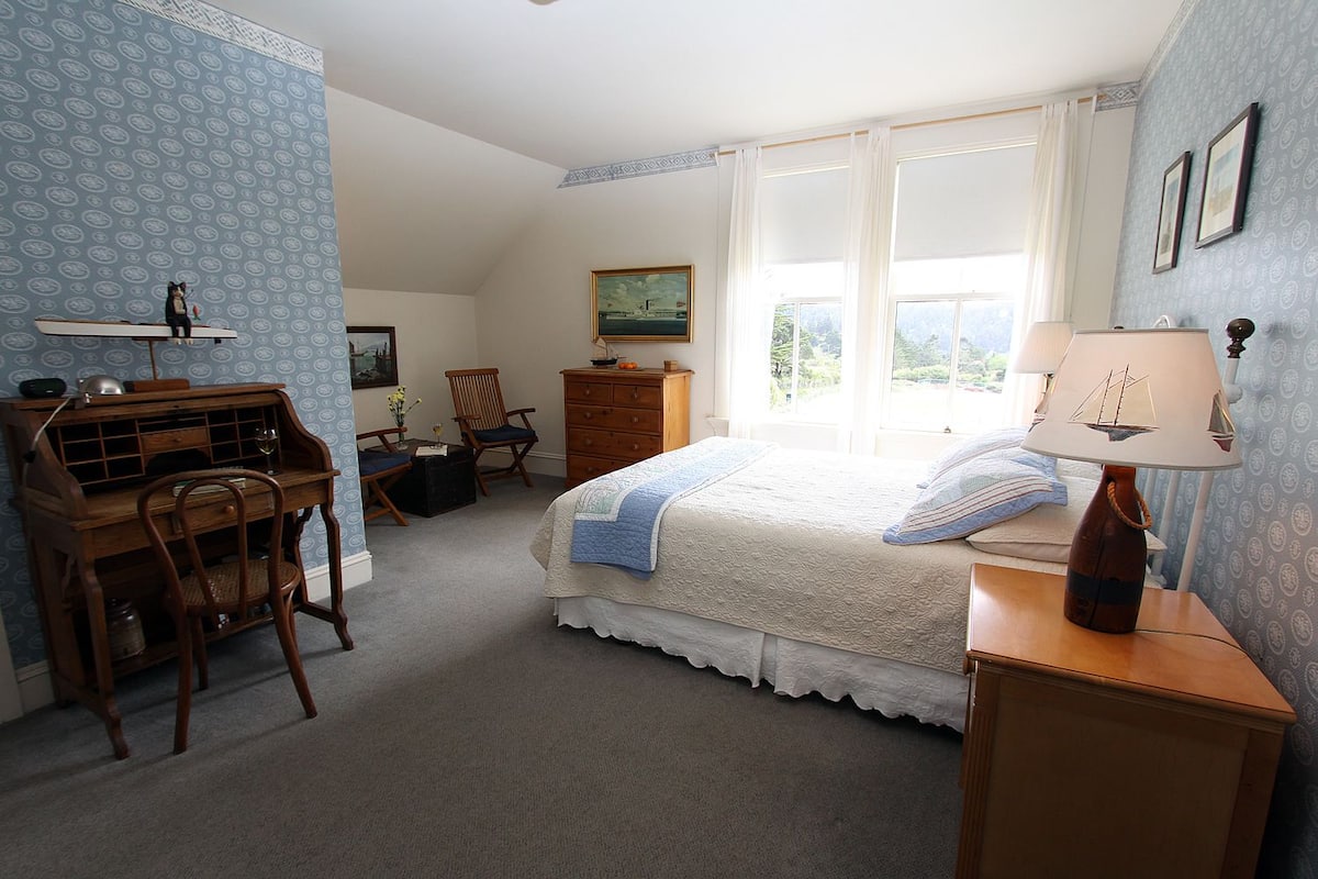 A bedroom with a bed, a desk, a chair, a dresser, and a lamp.