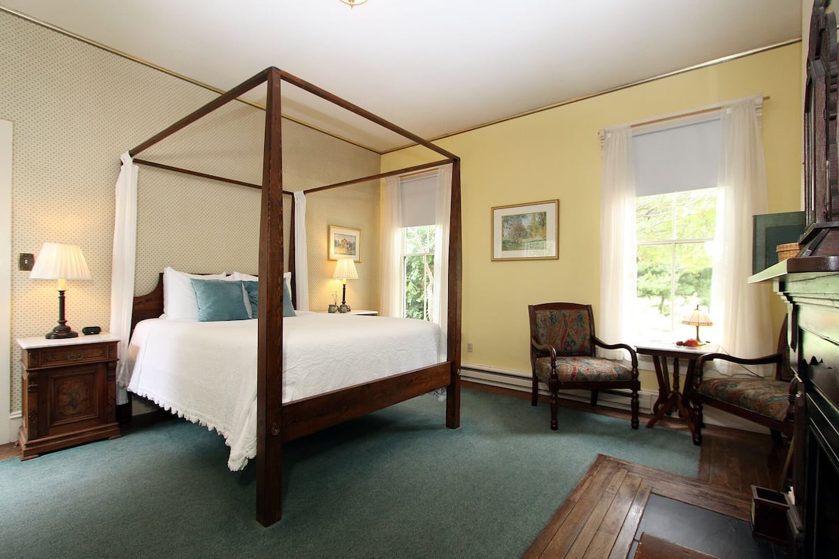 A four-poster bed with a canopy, a chair, a small table, and a fireplace.