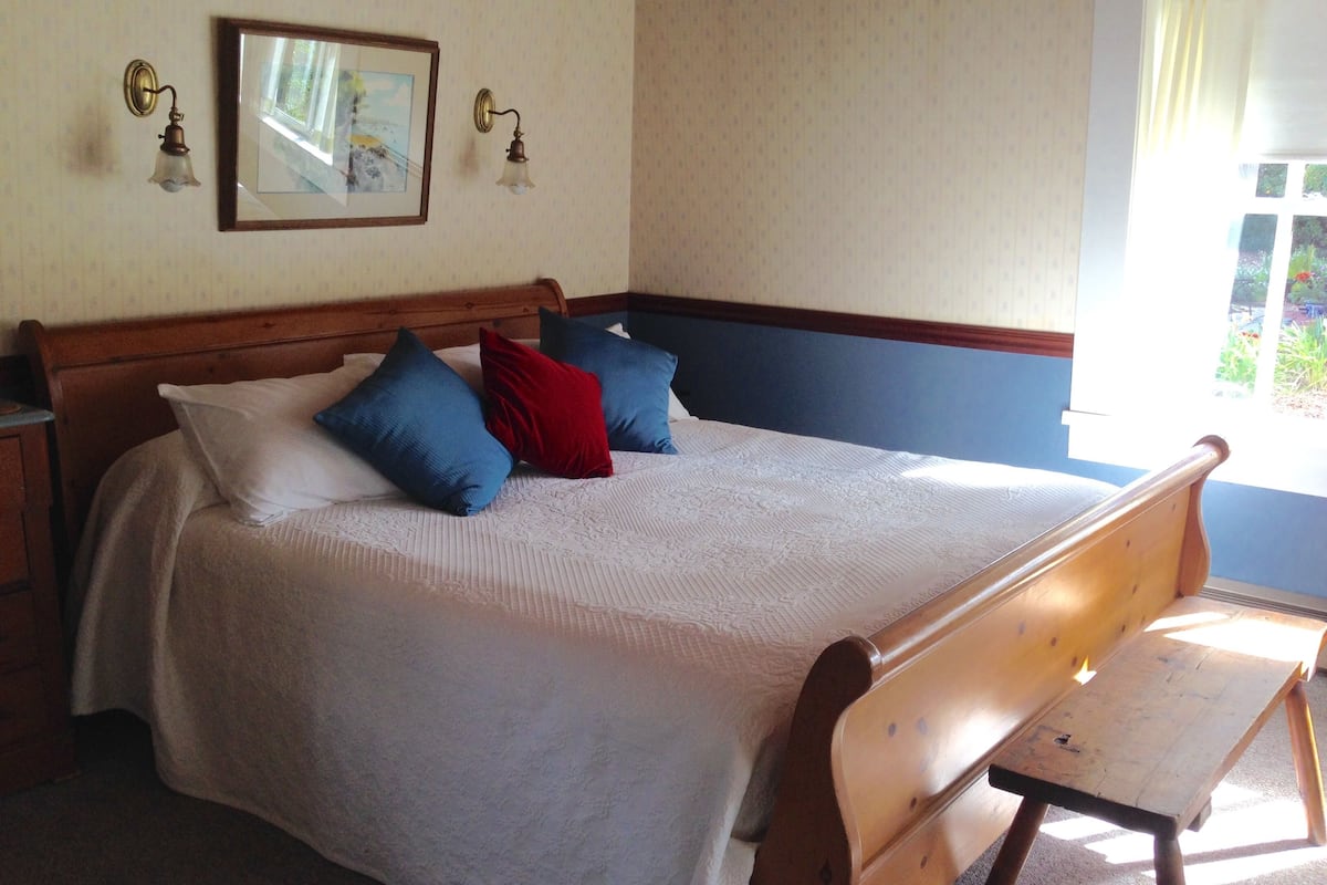 A neatly made bed with a wooden headboard, a wooden bench, and two wall-mounted light fixtures.