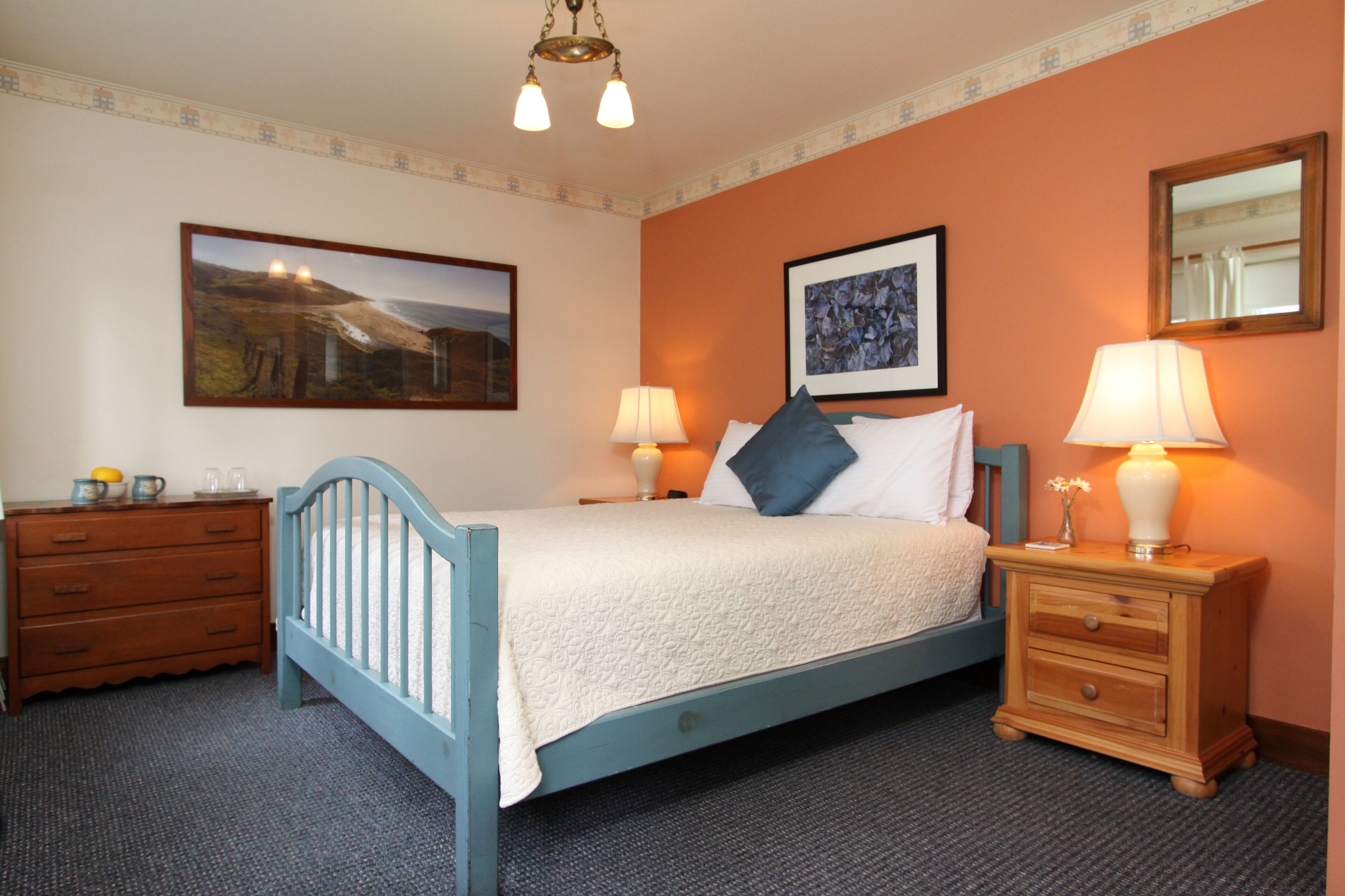 A bedroom with a bed, two bedside tables, a dresser, and two wall-mounted lamps.
