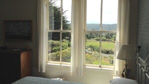 A bedroom with a large window, a bed, a nightstand, and a lamp. - Joshua Grindle Inn (Mendocino)