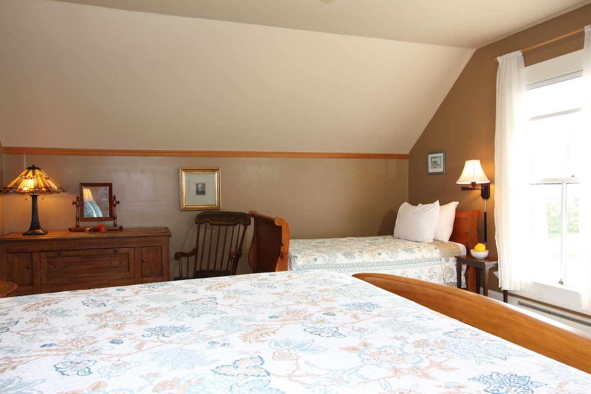 A bedroom with two beds, a dresser, a chair, and a window with curtains.