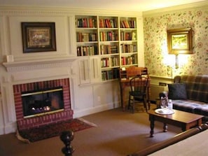 A cozy living room with a fireplace, a bookshelf, a plaid sofa, and a coffee table.