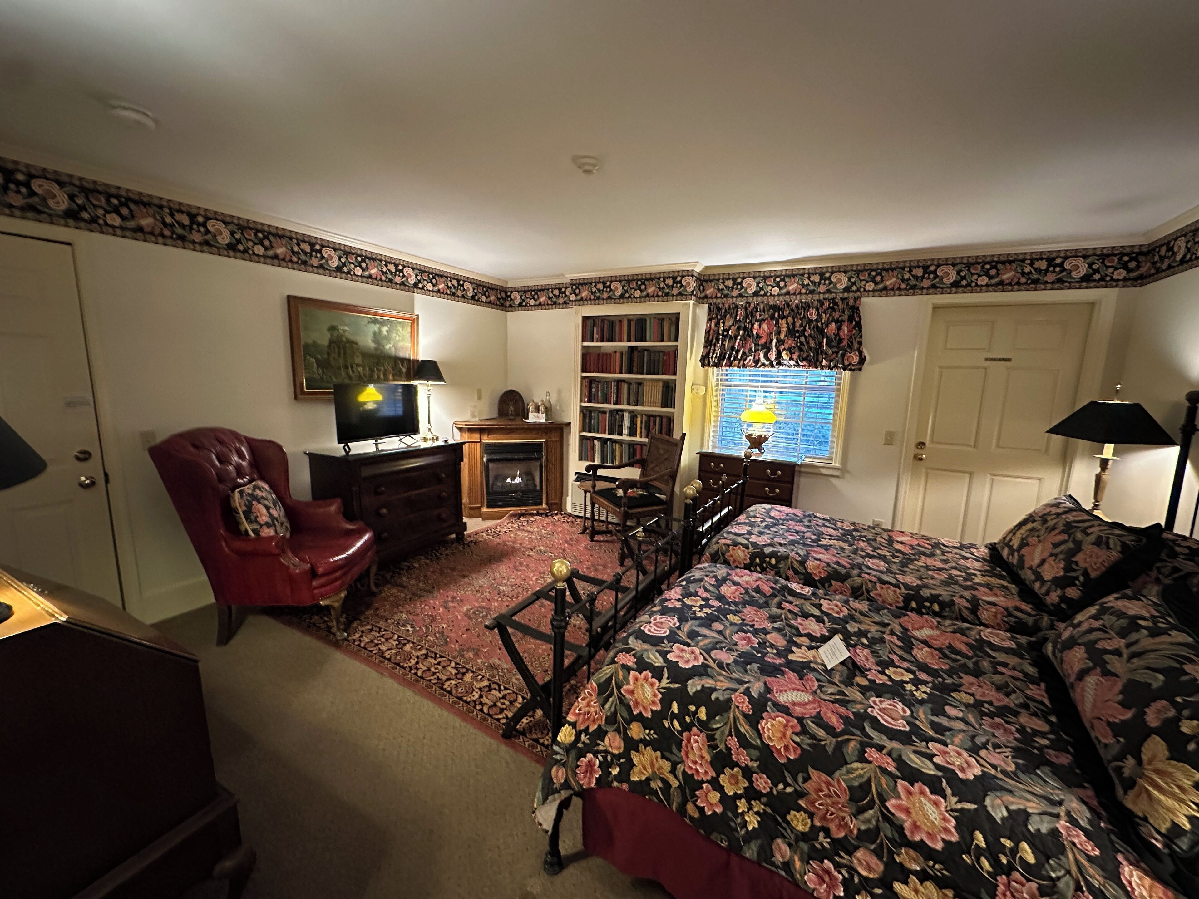 A bedroom with a bed, a desk, a chair, a fireplace, and a bookshelf.