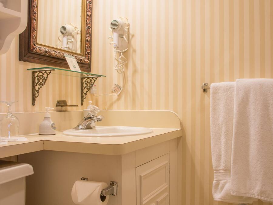 Un baño con pared a rayas, un espejo con marco decorativo, un lavabo con dispensador de jabón, una toalla colgada en la pared y un inodoro.
