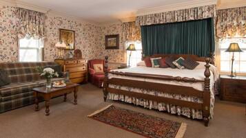 A traditional bedroom with a four-poster bed, a sofa, a wooden dresser, and a floral-patterned carpet.