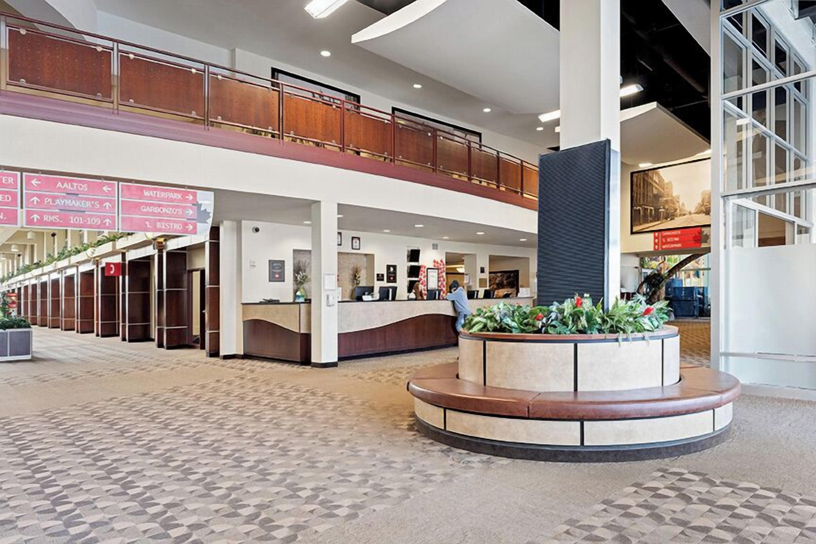 A hotel lobby with a central reception desk, a lower level with a balcony, and directional signs.