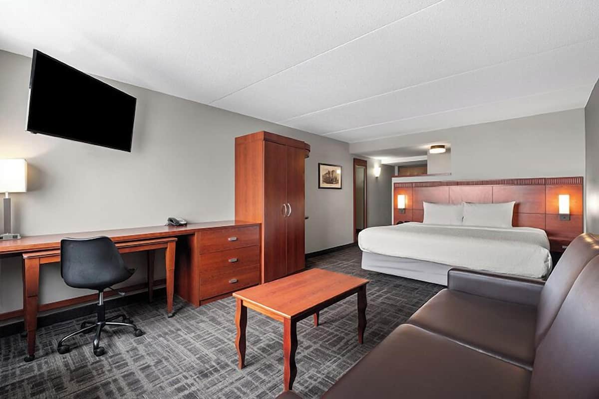 A hotel room with a bed, desk, chair, and a television mounted on the wall.
