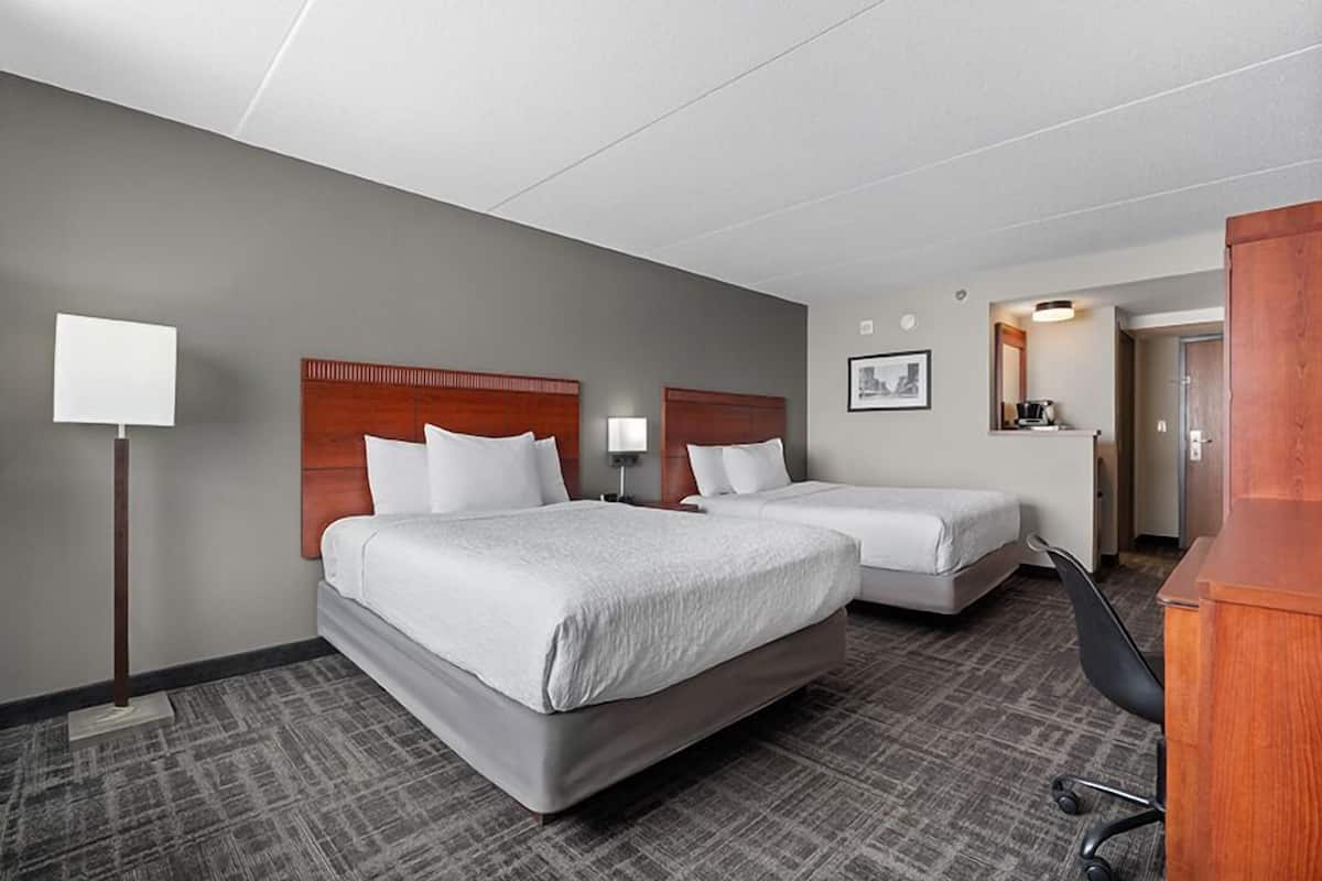 A hotel room with two beds, a desk, a chair, a lamp, and a picture on the wall.
