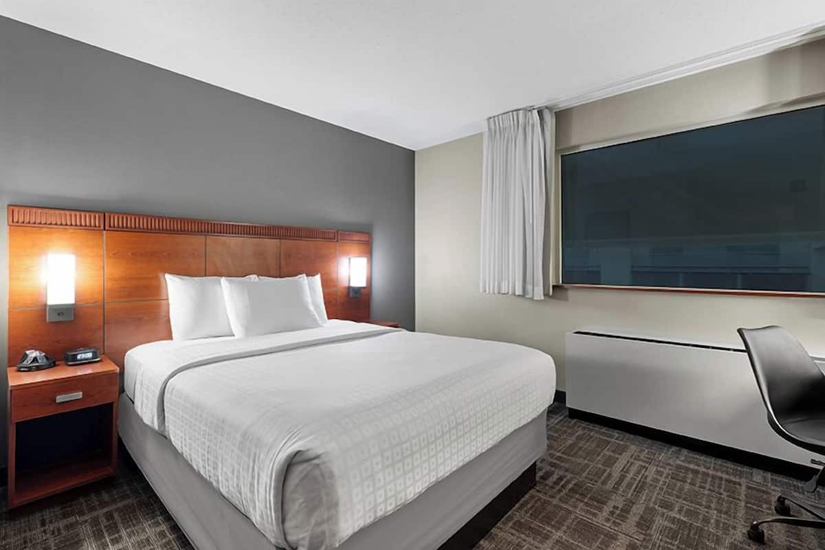 A hotel room with a large bed, bedside tables, a desk, and a window with curtains.