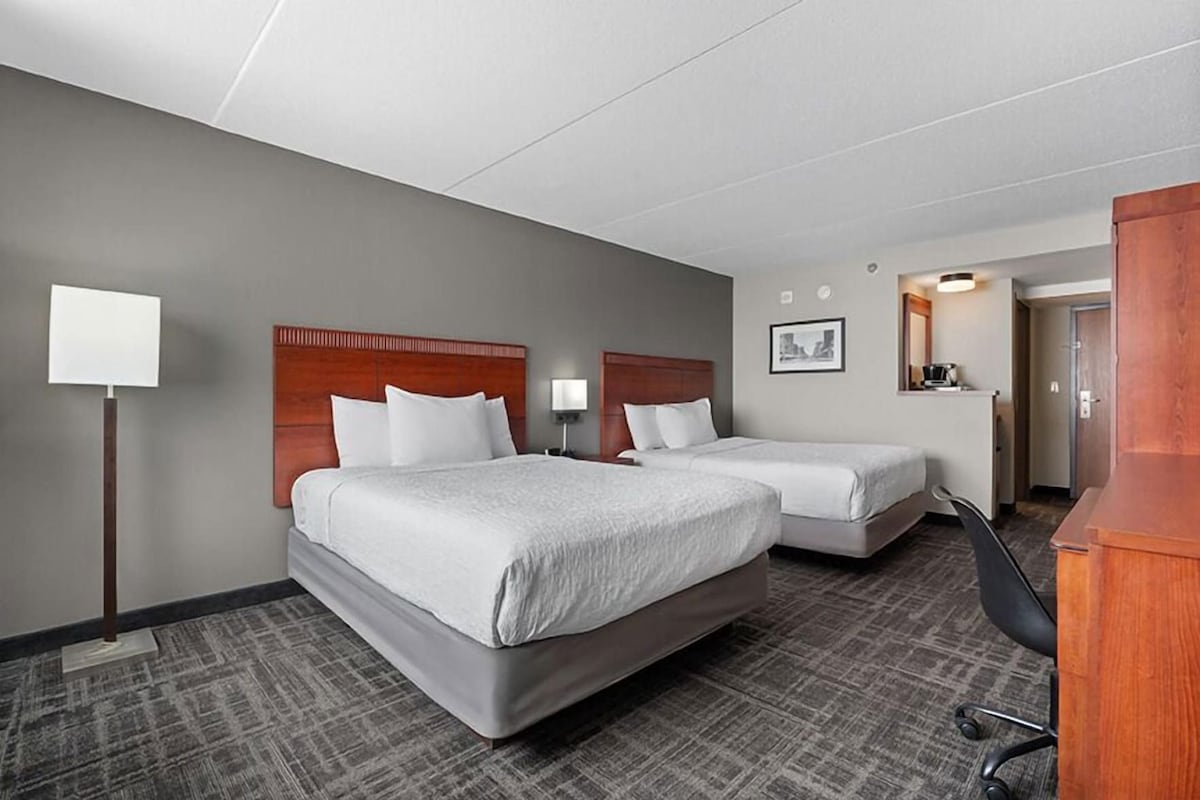 Une chambre d’hôtel avec deux lits, un bureau, une chaise, une lampe et un miroir.